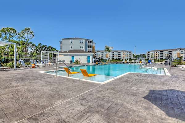 A large swimming pool surrounded by orange chairs and apartment buildings in the background.